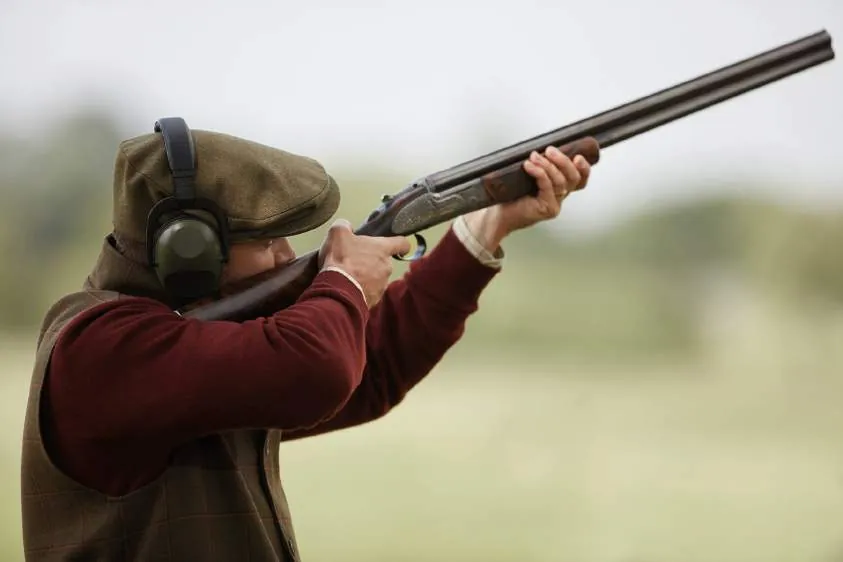 A shooter in a flat cap with a side-by-side gun